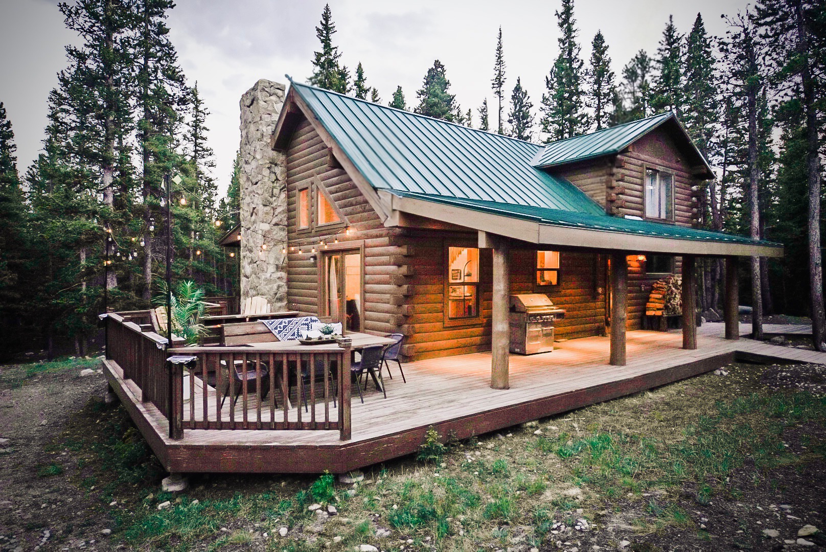 Timber Valley Lodge log cabin with green metal roof, stone chimney and deck dining in the pines